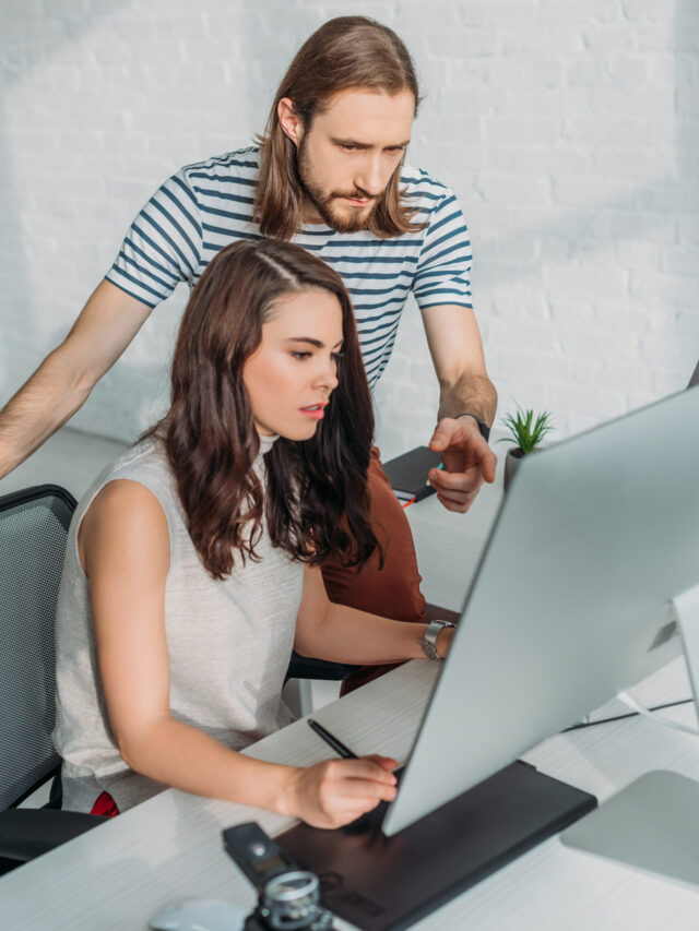 bearded art editor pointing with finger at computer monitor near attractive woman